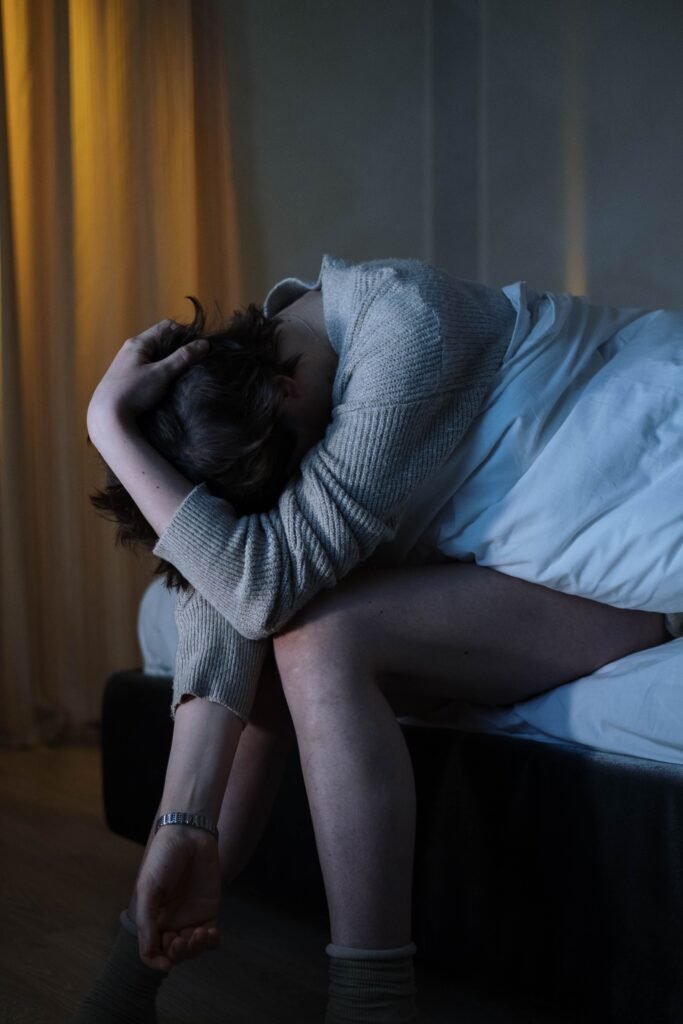 Pessoa sentada na beira da cama, com o corpo curvado e postura de cansaço emocional, simbolizando possível quadro depressivo.